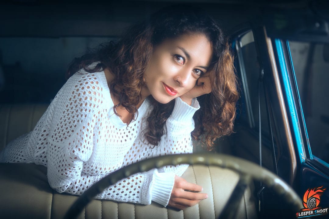 La modelo esta ubicada en la silla trasera apoyada en el espaldar de la silla delantera de un carro antiguo